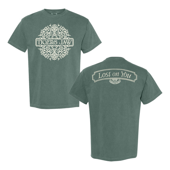 A sage green Tigers Jaw Comfort Colors T-shirt with ornate white band text on the front. The back features a crisp white 