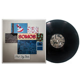 A vinyl record beside its album cover, featuring the brand name Somos, collage artwork with various images like a black backpack, and the album title First Day Back handwritten at the bottom.