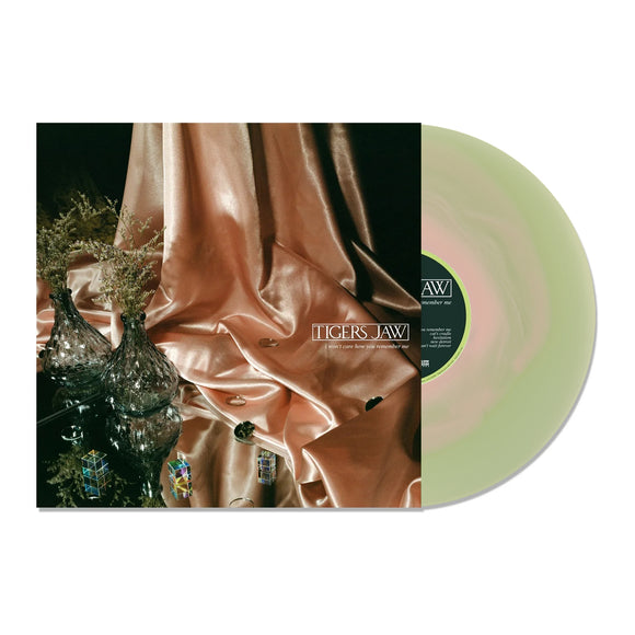 A pale green limited edition vinyl by Tigers Jaw partially slides out from its cover, which features glass vases, plants, shiny fabric, and small glass objects on a reflective surface. The cover displays the Tigers Jaw brand name.