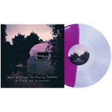A split purple and clear vinyl from Aaron West and the Roaring Twenties rests by its album cover, which features an Airstream trailer among dusk-lit trees in Monongahela Park, reading “In Lieu of Flowers.”.