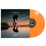 An orange vinyl record by The Wonder Years partially slides from an album cover featuring a sunset, a silhouette with their reflection on water, and the text "The Wonder Years – The Hum Goes On Forever." Ideal for orange vinyl collectors.
