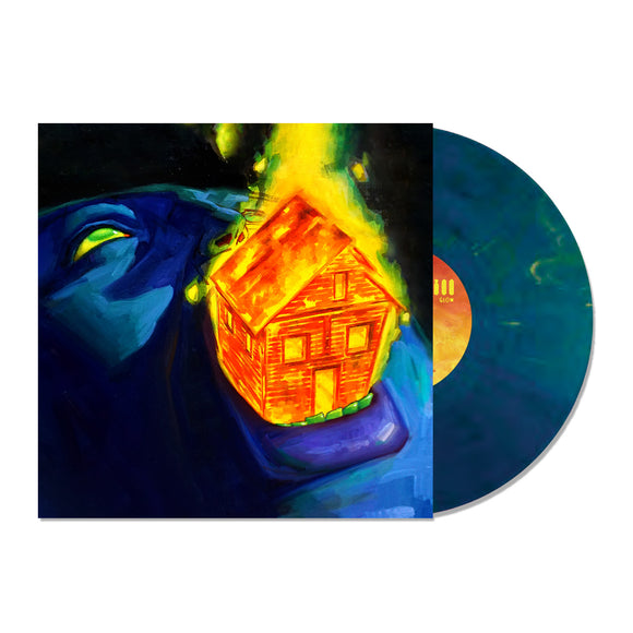 A vinyl record partially slides out of its cover, depicting a glowing house held in a blue hand on a dark background. The Sweet Pill Still There’s a Glow LP is dark blue with yellow and green marbling—a Gold Cobalt Blend.