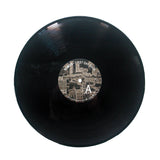 A black vinyl record by Somos with a center label showing a sepia cityscape, the text First Day Back, a large letter A, and a subtle Black Backpack motif on the right side.