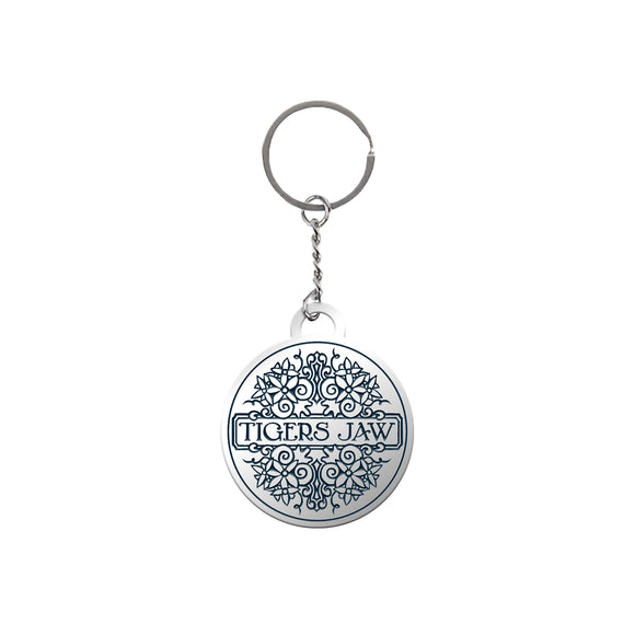 A round keychain featuring the Tigers Jaw brand name in the center, with an intricate engraved design and attached to a silver key ring.