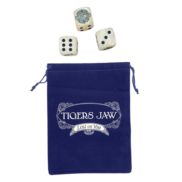 A blue velvet pouch branded Tigers Jaw rests beneath three custom dice, each displaying different numbers, neatly arranged above the bag.